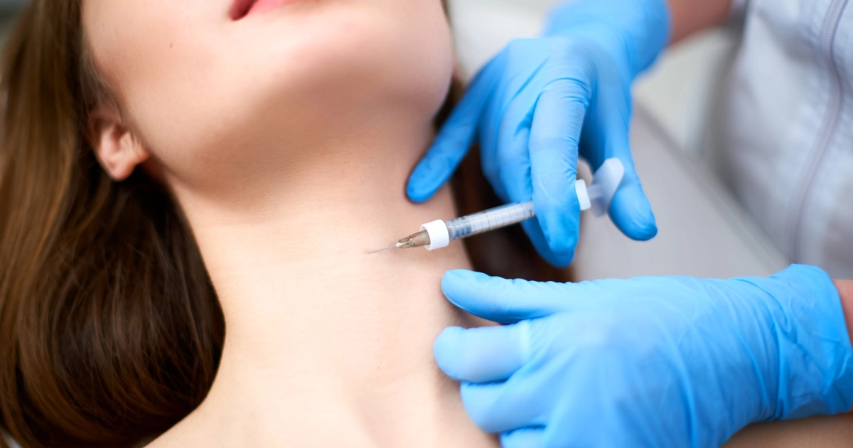 A close-up of a person receiving a cosmetic injection in their neck for a Neck Lift in Celebration, FL, from a healthcare professional wearing blue gloves.